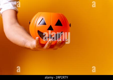 Mano che tiene una zucca arancione di Halloween su uno sfondo giallo, chiedendo caramelle Foto Stock