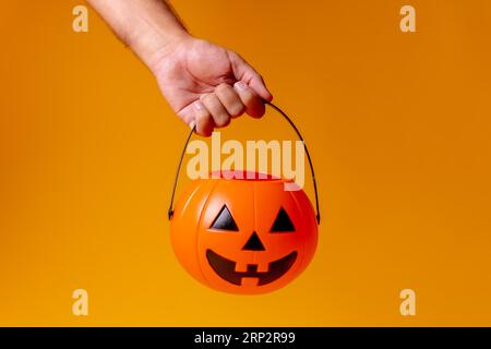 Mano che tiene una zucca arancione di Halloween su uno sfondo giallo, chiedendo caramelle Foto Stock