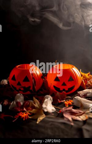 Zucche di Halloween su foglie autunnali e fantasmi con fumo su sfondo nero, copia e incolla spazio Foto Stock