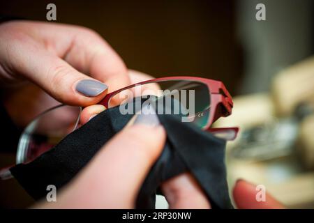 Una donna pulisce un paio di occhiali e lenti da vista Foto Stock