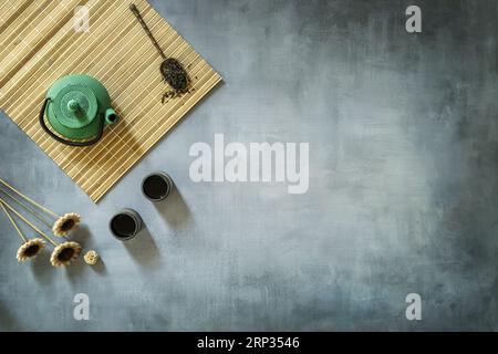 Una natura morta di piccole tazze da tè con tè secco, alcuni fiori secchi e una teiera su un rack di bambù Foto Stock