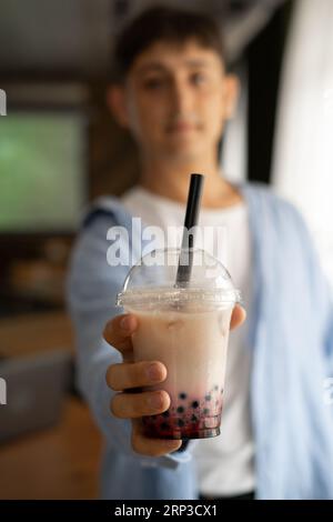 Uomo che tiene in mano il tè bollicine di latte ghiacciato con perle di tapioca e lo mostra alla macchina fotografica, bevanda tradizionale di Taiwan. Foto Stock