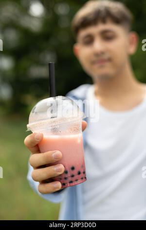 Il giovane beve tè bollicine e si goda le vacanze estive mostrando una tazza di plastica sulla fotocamera Foto Stock