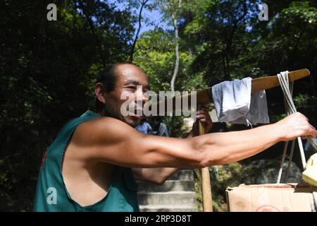 (181001) -- HUANGSHAN, 1 ottobre 2018 -- Heaver Wu Xiaofu si prende una pausa dal lavoro nell'area panoramica di Huangshan Mountain nella città di Huangshan, nella provincia di Anhui della Cina orientale, 30 settembre 2018. Wu Xiaofu, 53 anni, lavora come heaver da 18 anni. Il suo lavoro è quello di trasportare carichi di provviste, solitamente di peso superiore a 50 chilogrammi, con un palo di bambù sulle spalle dai piedi del monte Huangshan fino agli hotel e ai negozi in cima alla montagna. Secondo Wu, scalare la montagna con carichi pesanti sulle spalle richiede non solo molta forza corporea, ma anche una buona padronanza del ritmo e del sp Foto Stock