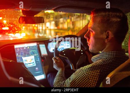 Guida Uber al volante di un veicolo elettrico Tesla di notte sotto la pioggia Foto Stock