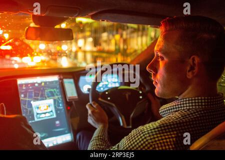 Guida Uber al volante di un veicolo elettrico Tesla di notte sotto la pioggia Foto Stock