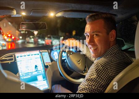 Guida Uber al volante di un veicolo elettrico Tesla di notte sotto la pioggia Foto Stock