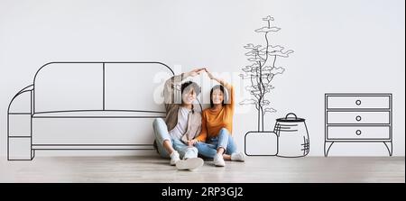 Coppia asiatica millenaria sorridente che fa il tetto con le mani sul pavimento, compra casa, isolata su sfondo bianco Foto Stock