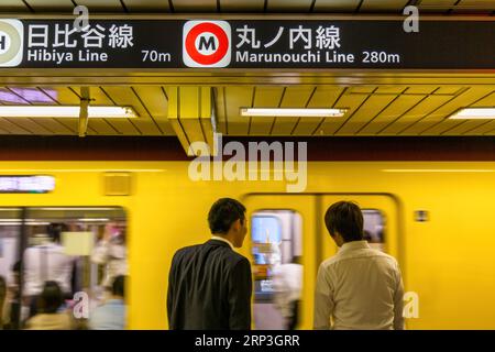 Tokyo, Giappone - 22 giugno 2023: I pendolari attendono un treno della metropolitana della linea JR da una stazione della metropolitana di Tokyo. Attenzione selettiva alla segnaletica per Marunouchi e. Foto Stock