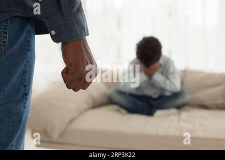 Padre nero stringendo pugno minacciando figlio spaventato a casa, tagliato Foto Stock