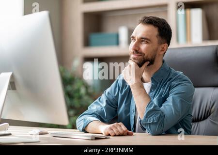 Bell'imprenditore maschile seduto sul posto di lavoro con espressione riflessiva del volto Foto Stock