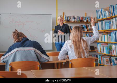 Studentesse che alzano le mani durante l'istruzione in classe, comunicando con una insegnante sorridente Foto Stock