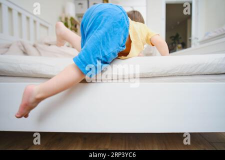 Il bambino sta salendo sul letto alto, c'è il rischio che cada. Bimbo di due anni (bimbo di due anni) Foto Stock