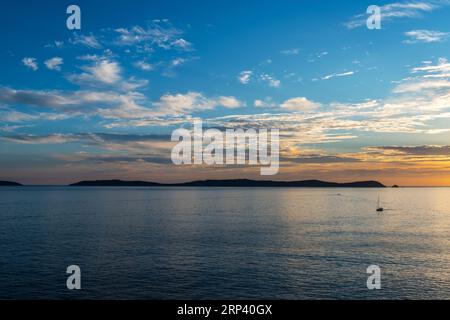 Una barca solitaria naviga lontano dall'isola di Ons nella Ria de Pontevedra in Galizia durante il tramonto. Queste isole sono state designate area di protezione speciale per Foto Stock