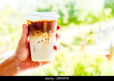 Primo piano di una persona che tiene in mano un rinfrescante macchiato a strati di caffè ghiacciato in una tazza di plastica trasparente con coperchio Foto Stock