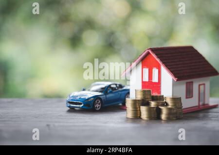 Coppia in miniatura in piedi sul denaro delle monete d'oro con casa modello e auto su sfondo verde naturale, risparmia denaro per prepararti in futuro e pensionamento co Foto Stock