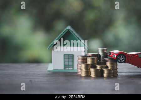 Coppia in miniatura in piedi sul denaro delle monete d'oro con casa modello e auto su sfondo verde naturale, risparmia denaro per prepararti in futuro e pensionamento co Foto Stock