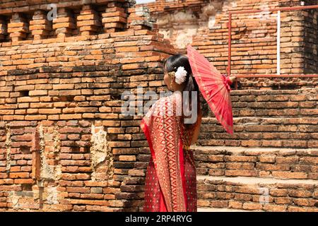 una donna asiatica che indossa un tradizionale abito tailandese sta in piedi con ombrello contro il vecchio tempio di ayutthaya, patrimonio mondiale dell'unesco in thailandia. Ayutthaya, Thailandia M. Foto Stock