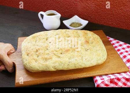 Mettere a mano il delizioso pane alla focaccia alle erbe appena sfornato sul tavolo Foto Stock
