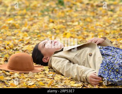 (181126) -- NANCHINO, 26 novembre 2018 -- Una ragazza giace sulle foglie di ginkgo cadute nel parco Binjiang a Nanchino, capitale della provincia di Jiangsu della Cina orientale, 25 novembre 2018. ) (yy) CHINA-AUTUMN-GINKGO (CN) YangxSuping PUBLICATIONxNOTxINxCHN Foto Stock