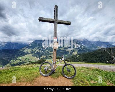 3 settembre 2023, Dienten am HochkÃÂ¶nig, Land Salzburg, Austria: Una mountain bike si appoggia contro una Gipfelkreuz (croce sommitale) con uno sfondo delle famose montagne HochkÃÂ¶nig (Hochkoenig) nel Land Salzburg, Austria. (Immagine di credito: © Sachelle Babbar/ZUMA Press Wire) SOLO USO EDITORIALE! Non per USO commerciale! Foto Stock