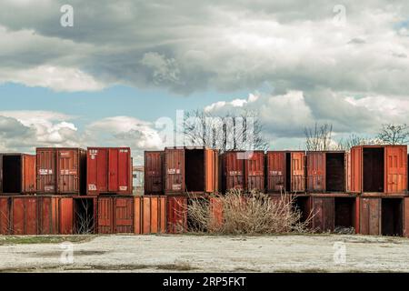 Una lunga fila di contenitori metallici vuoti su un sacco di pavimenti sabbiosi Foto Stock