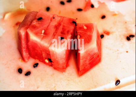 Pochi pezzi di anguria con semi e succo sulla tavola da cucina, primo piano. Foto Stock