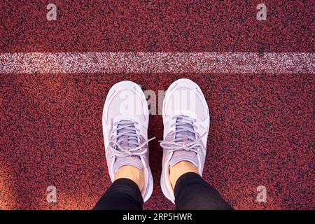 Scarpe sportive di una donna in piedi su un parco giochi rosso o su una pista da corsa dietro una linea bianca, vista dall'alto Foto Stock