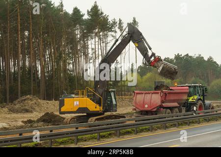 Lavori di riparazione su strada. L'escavatore carica la massa nel rimorchio del trattore. Foto Stock