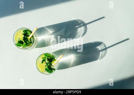 Due bevande mojito con cannucce sul tavolo blu. Bevande rinfrescanti fredde. Ombre lunghe e dure. Vista dall'alto, base piatta. Foto Stock