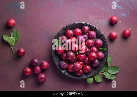 Prugne di ciliegia rosse dolci su piatto nero. Foto Stock