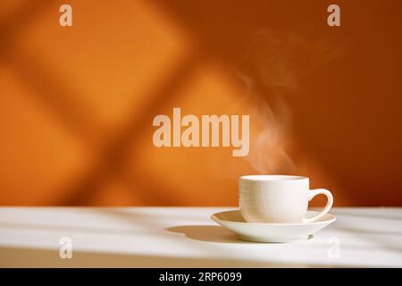 Primo piano della tazza di caffè sul tavolo alla luce diretta del sole. Caffè mattutino con vapore in tazza bianca. Foto Stock
