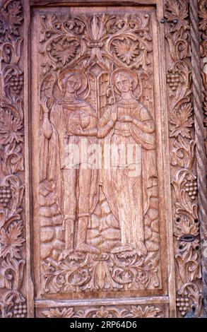 Moldavia, Romania, circa 2000. Porta in legno splendidamente intagliata all'entrata di una chiesa locale. Dettaglio di una rappresentazione degli Arcangeli Michael e Gabriel. Foto Stock