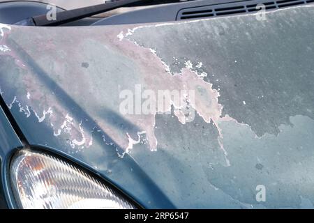 Distacco della vecchia vernice di un cofano auto blu da vicino danneggiato Foto Stock