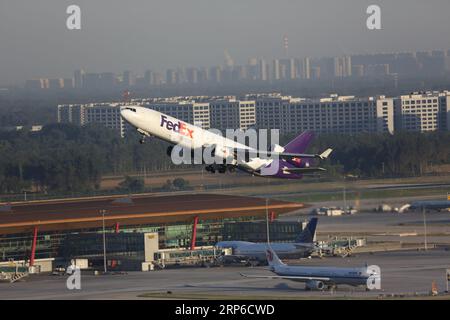 Un aereo FedEx decolla da una pista trafficata in una città vivace, fornendo servizi di consegna dei pacchi all'area circostante Foto Stock