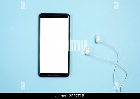 Telefono cellulare con schermo bianco con auricolari su sfondo blu Foto Stock