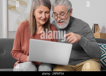 Elderly couple with laptop discussing pension plan in room Foto Stock