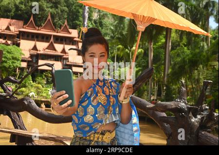 Bellissima donna tailandese in costume nazionale che scatta un selfie con il suo telefono cellulare. Foto Stock