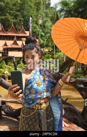 Bellissima donna tailandese in costume nazionale che scatta un selfie con il suo telefono cellulare. Foto Stock