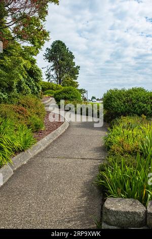 Particolare di un giardino botanico. Sentiero in pietra con erba che cresce lungo il giardino. Passerella nel giardino fiorito in estate. Sentiero per correre, camminare, cy Foto Stock