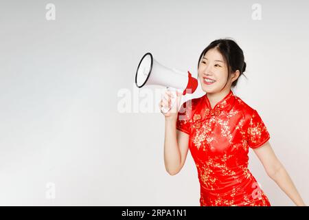 Donna asiatica che indossa un tradizionale abito qipao cheongsam con gesto che regge il megafono isolato su sfondo bianco. Felice anno nuovo cinese. Foto Stock