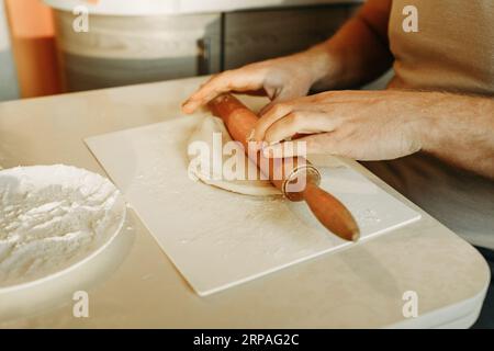 Un uomo stende l'impasto con un matterello, cucina a casa. Primo piano. Foto Stock