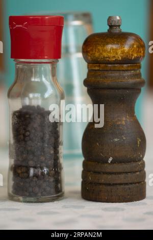 tritatutto in legno accanto a una confezione di vetro di grani di pepe nero Foto Stock