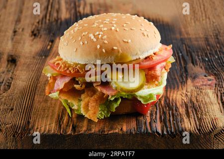 Hamburger di pollo Kentucky con cetriolo sottaceto e pomodoro fresco su fondo di legno Foto Stock