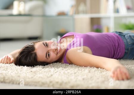 Una donna felice a casa che guarda la fotocamera sdraiata su un tappeto Foto Stock