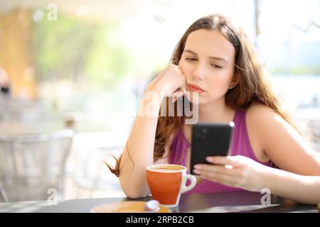 Donna frustrata che controlla lo smartphone in una terrazza del ristorante Foto Stock