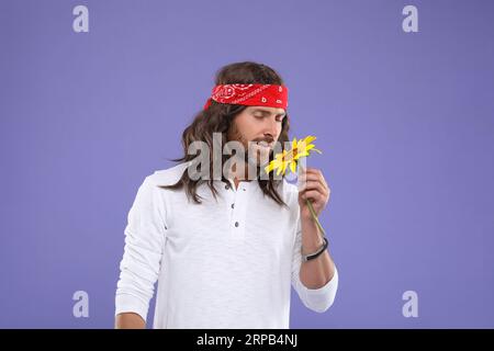 Elegante uomo hippie con girasole su sfondo viola Foto Stock