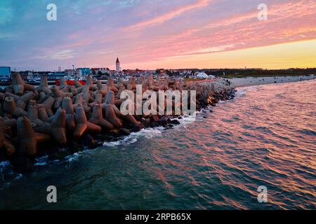 Le onde si infrangono sulle frangiflutti in cemento tetrapod sulla costa del mare. Protezione da onde grandi. Costa del Mar Baltico al porto di Wladyslavovo al tramonto Foto Stock