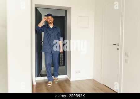 Un riparatore professionista in uniforme sta arrivando in casa con la cassetta degli attrezzi in mano Foto Stock