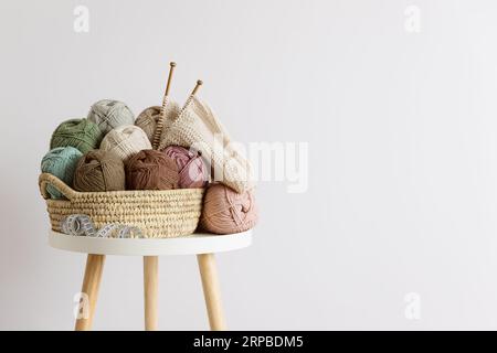 Lana naturale in palle di vari colori pastello in un cestino di vimini sul tavolo. Copia spazio. Foto Stock